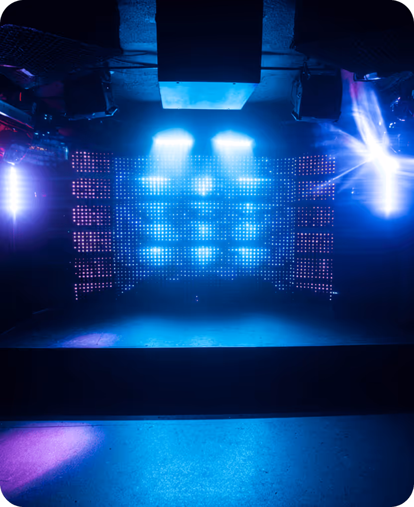 Empty stage with vibrant blue and purple LED lights and spotlights in a dark entertainment venue.