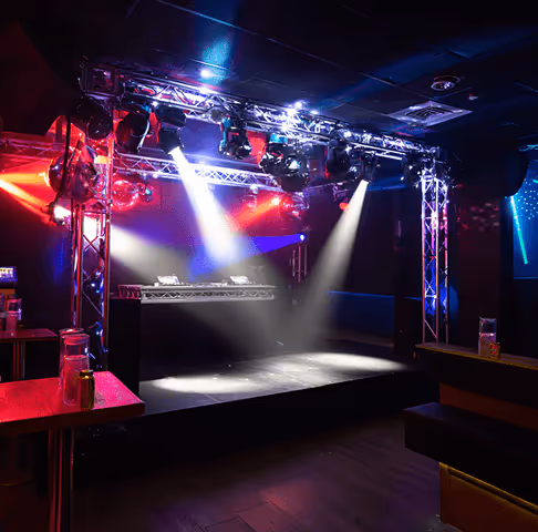 Empty nightclub stage with colorful spotlights and DJ equipment under metal truss lighting rig.