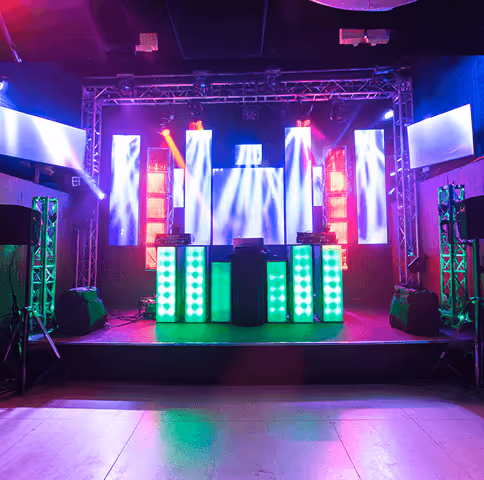 Empty DJ stage setup with colorful LED screens and lighting effects in a dark club room.