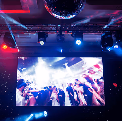 Large screen displaying a blurred image of people dancing at a party under colorful stage lights and a disco ball.