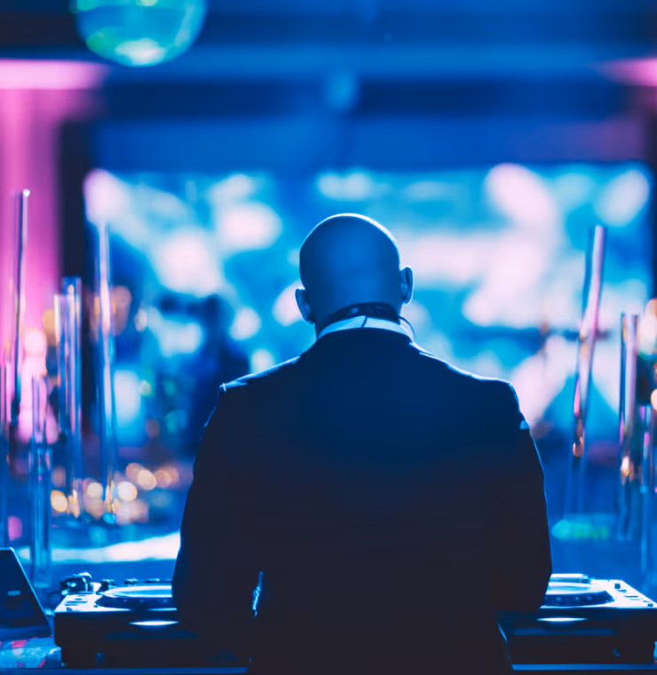 Bald DJ in a suit performing at a nightclub with blue and purple lights.