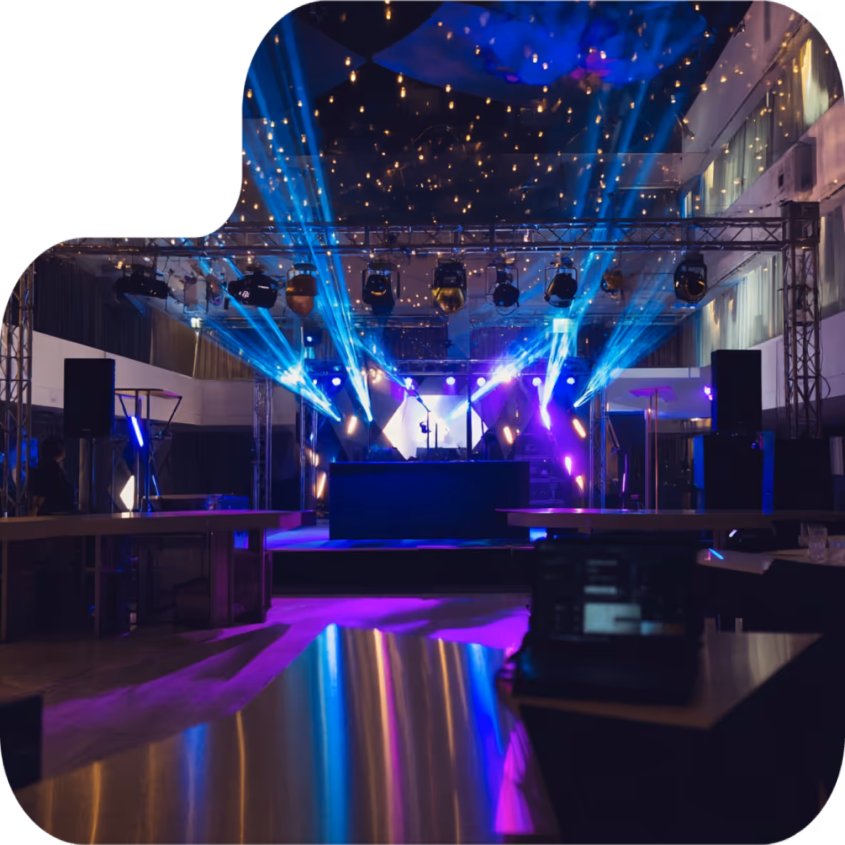 Indoor event stage with blue and purple spotlights and string lights on the ceiling.