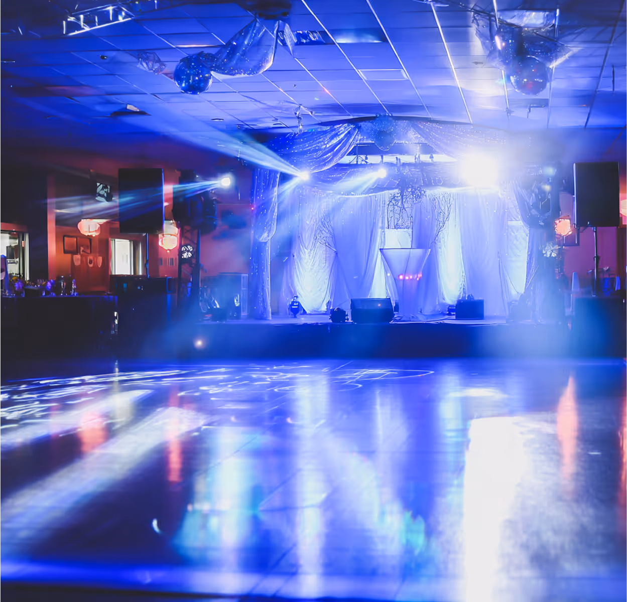 Empty event stage decorated with draped curtains and blue spotlights illuminating the floor.