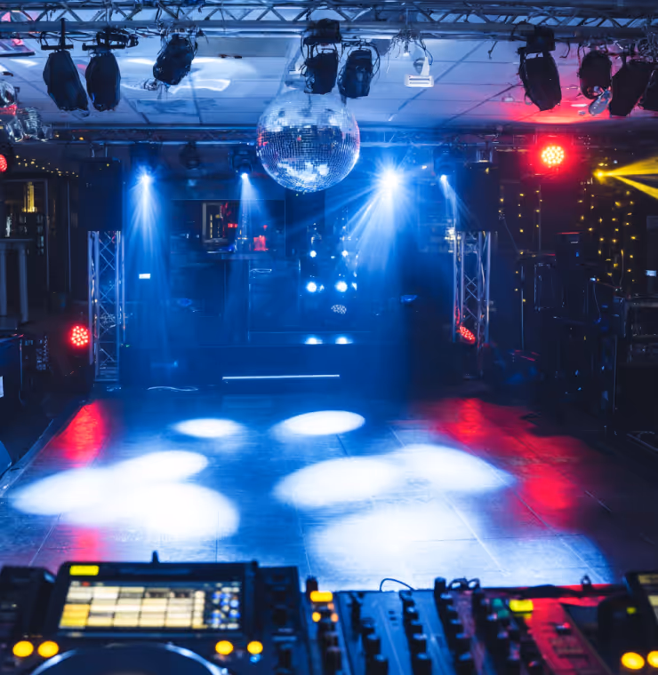 Empty nightclub dance floor illuminated by blue, red, and yellow stage lights with a disco ball hanging from the ceiling.