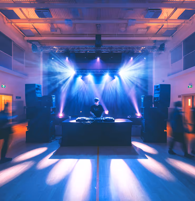 DJ performing on a stage with colorful bright spotlights in a large indoor venue.
