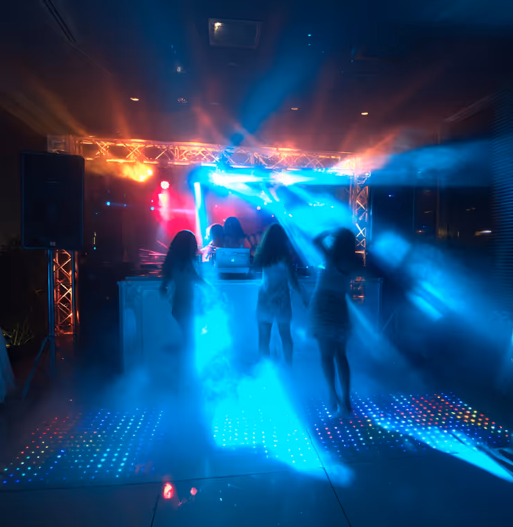 Silhouettes of four people dancing on a lighted dance floor with blue and orange stage lights and fog effects.