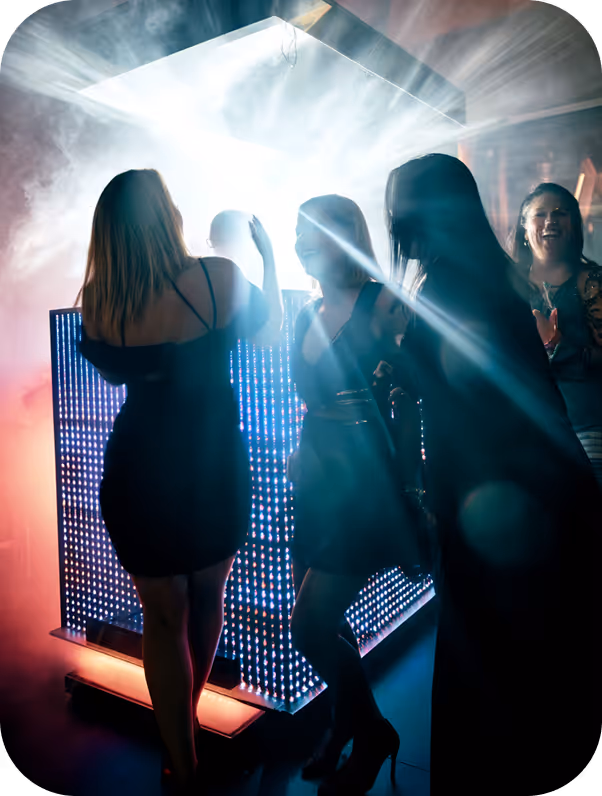 Group of women dressed in black dancing and enjoying at a nightclub with colorful LED lights and smoke effects.