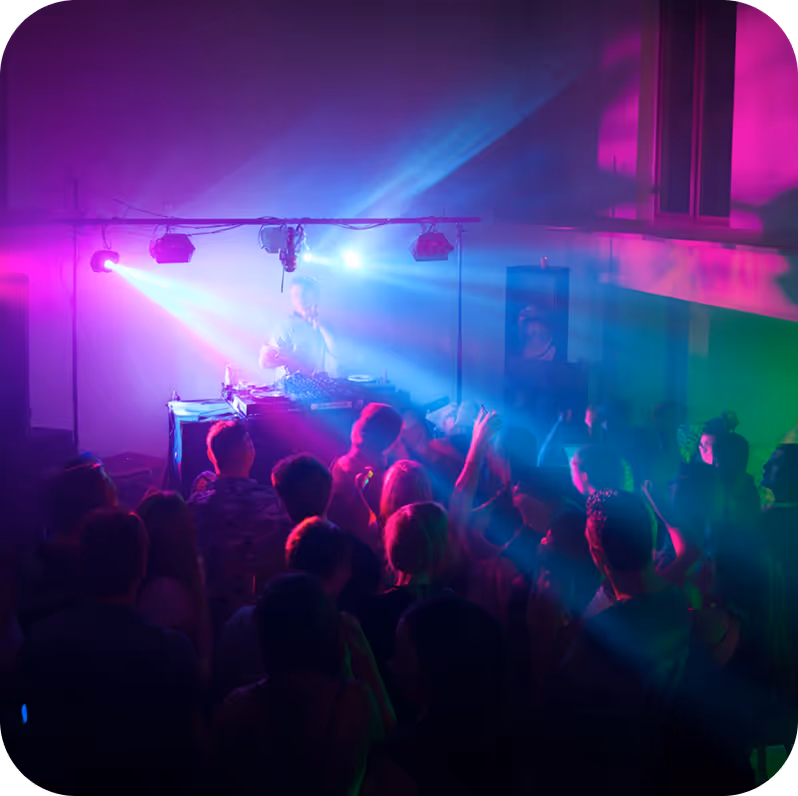 DJ performing with colorful purple and blue lights shining over a crowd dancing in a dark room.