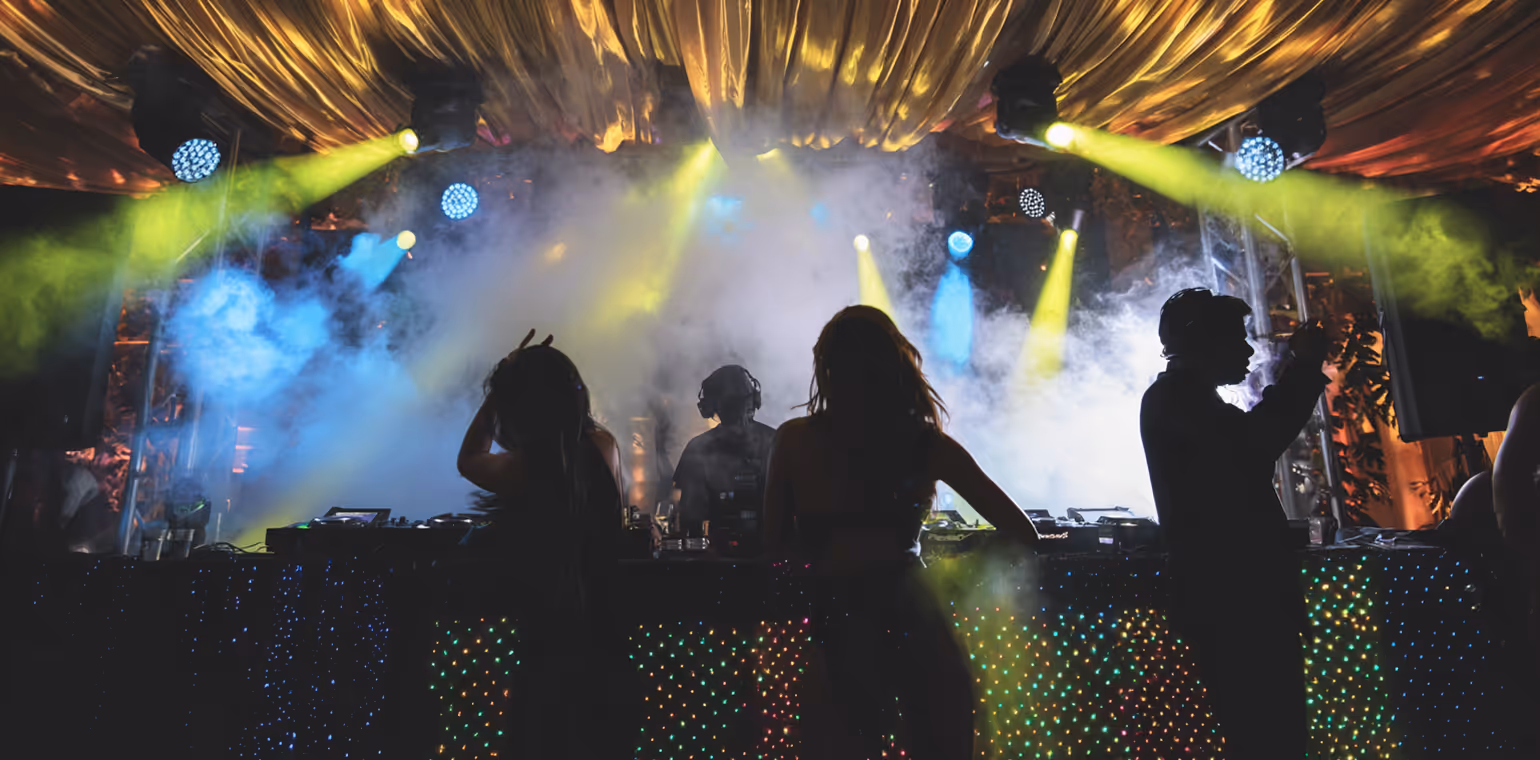 Silhouettes of three people dancing and a DJ performing on a stage with colorful lights and fog effects.