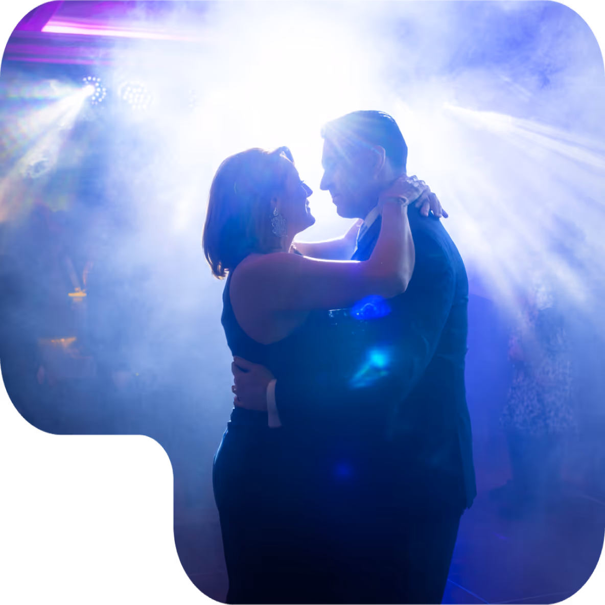 Couple dancing closely together in a dimly lit room with bright backlighting and smoke effects.