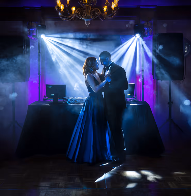 Couple elegantly dancing together on a dimly lit dance floor with blue and purple lighting and smoke effects.