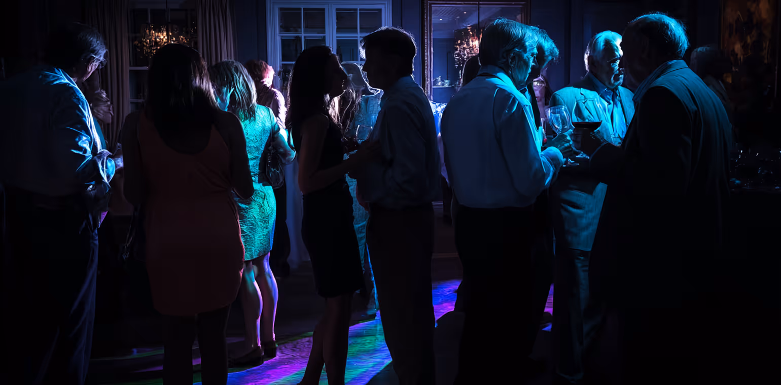 Group of people socializing and dancing in a dimly lit room with colorful floor lights.
