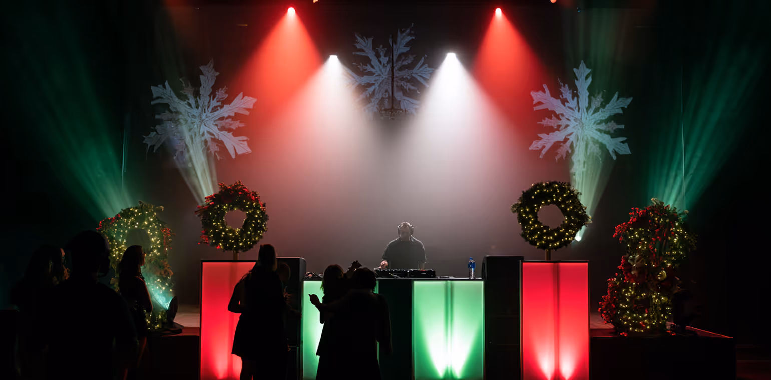 DJ performing on a lit stage decorated with Christmas wreaths and illuminated snowflake projections, with people dancing in front.