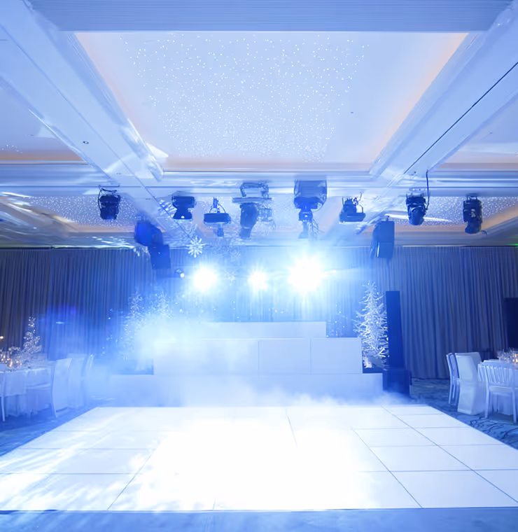 Empty white dance floor with bright stage lights and fog in a decorated event hall.