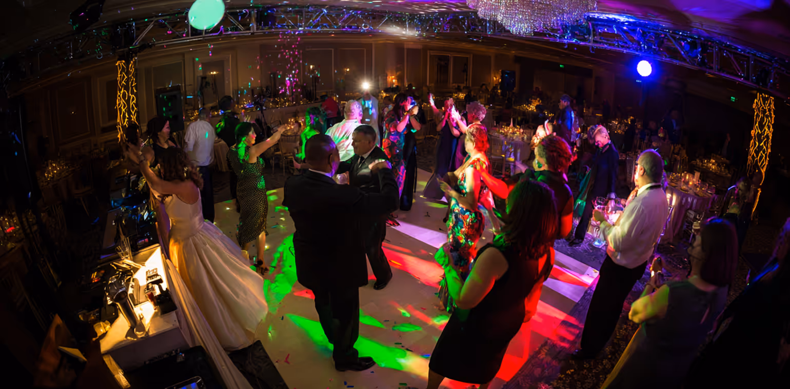 Guests dancing and socializing under colorful lights in an elegant ballroom with round tables set for a formal event.