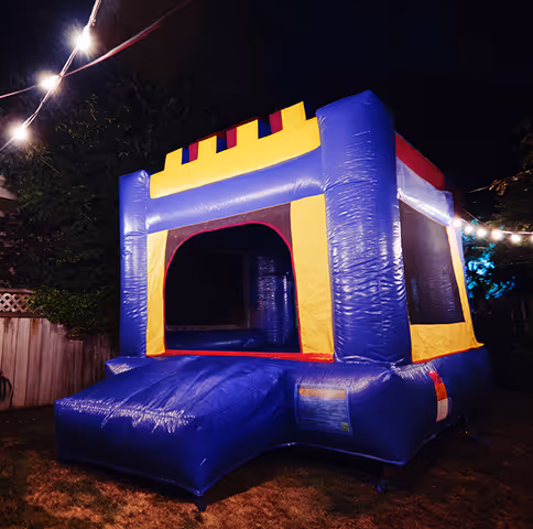 Inflatable blue and yellow bouncy castle set up outdoors at night with string lights overhead.