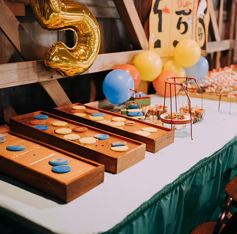 Table with wooden board games, colorful balloons, and a large gold number 5 balloon at a party.
