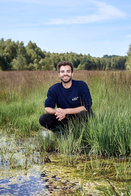 Lucas Gerrits, Gründer des Startup ZukunftMoor kniet vor einem Torfmoosfeld und lächelt in die Kamera