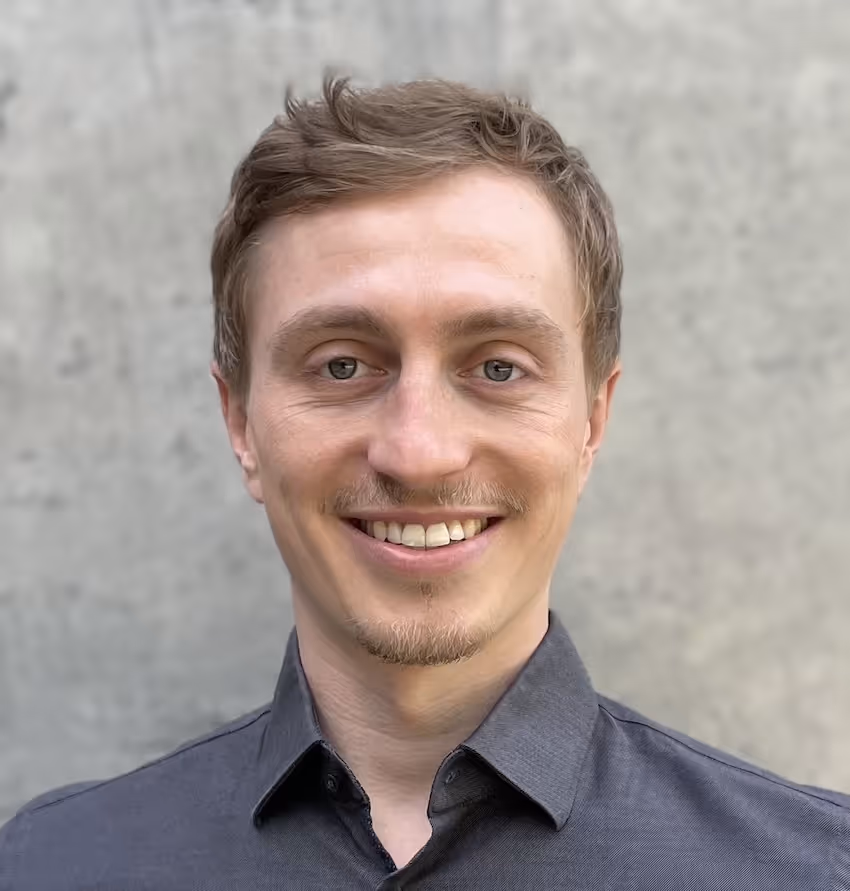 Ein junger Mann mit dunkelgrauem Hemd lächelt.