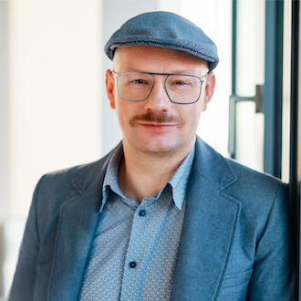 Portrait von einem Mann im Hemd, Sakko und Schiebermütze mit Oberlippenbart und Brille