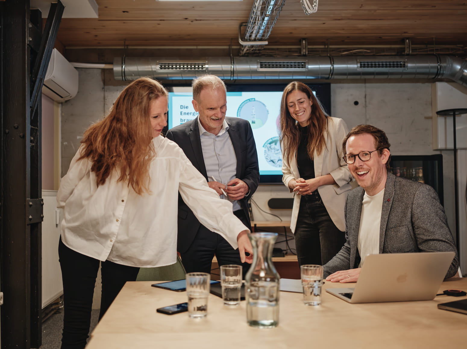Zwei Frauen und zwei Männer im Business-Outfit unterhalten sich angeregt und schauen dabei auf einen Laptop
