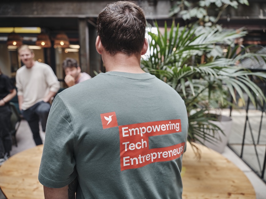 Ein Mann sitzt mit dem Rücken zur Kamera. Er trägt ein grünes Shirt mit orangenem Aufdruck.