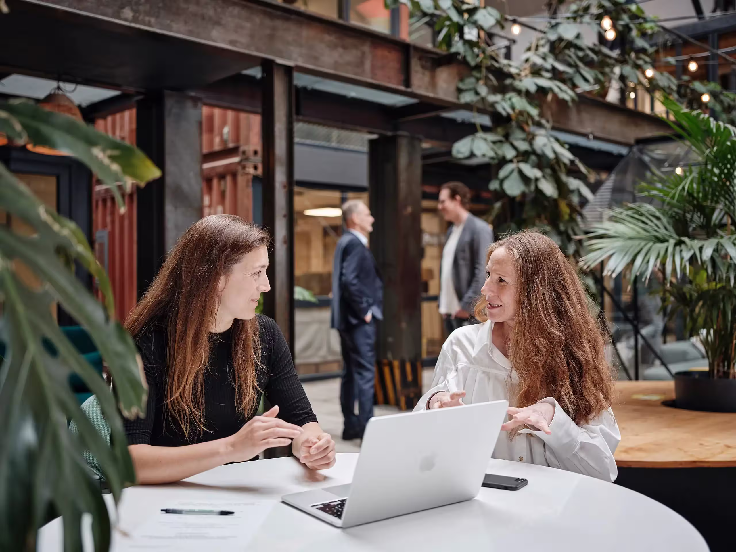 Zwei Frauen sitzen produktiv an einem Tisch vor einem Laptop und besprechen eine GreenTech Innovation.