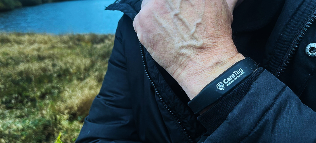 CareTag emergency ID kit showing a black NFC-enabled wristband and blue emergency ID card resting on a smartphone, used to access vital medical information in emergencies.