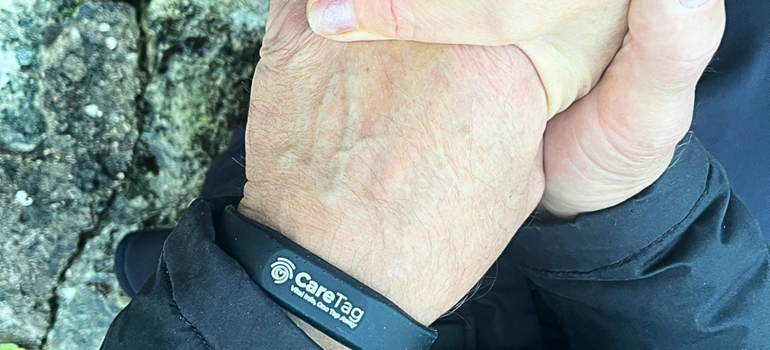 CareTag emergency ID kit showing a black NFC-enabled wristband and blue emergency ID card resting on a smartphone, used to access vital medical information in emergencies.