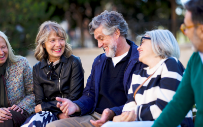 Group of older adults sitting outdoors together, smiling and chatting in a relaxed social setting.