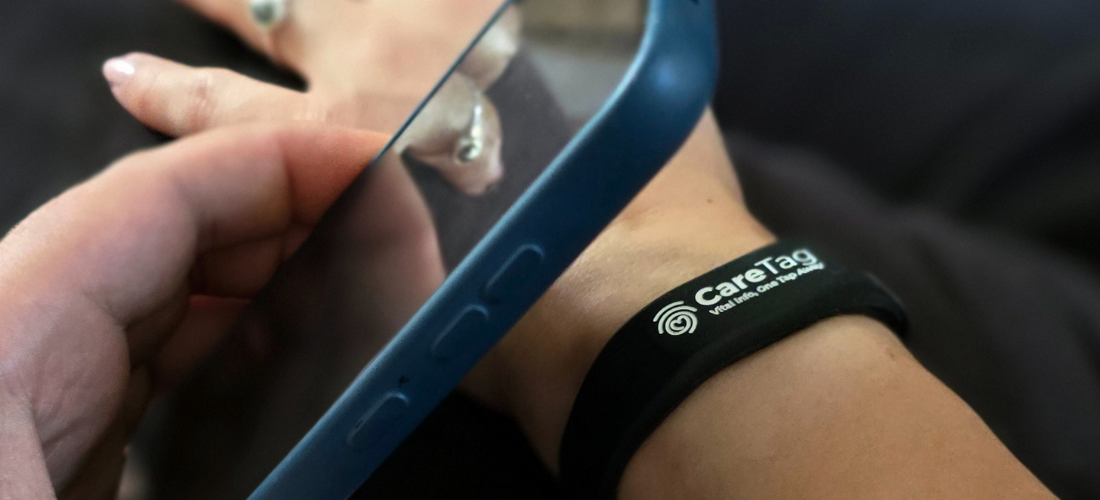 CareTag emergency ID kit showing a black NFC-enabled wristband and blue emergency ID card resting on a smartphone, used to access vital medical information in emergencies.