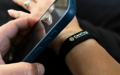 Person tapping a smartphone against a CareTag™ medical ID bracelet worn on the wrist to access emergency information.