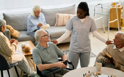 Carer supporting older adults in a social care setting, speaking with residents in a communal living area.