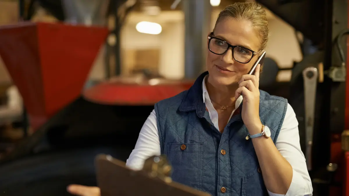 A woman in a warehouse making a phone call while reviewing a clipboard, representing the supplier onboarding process
