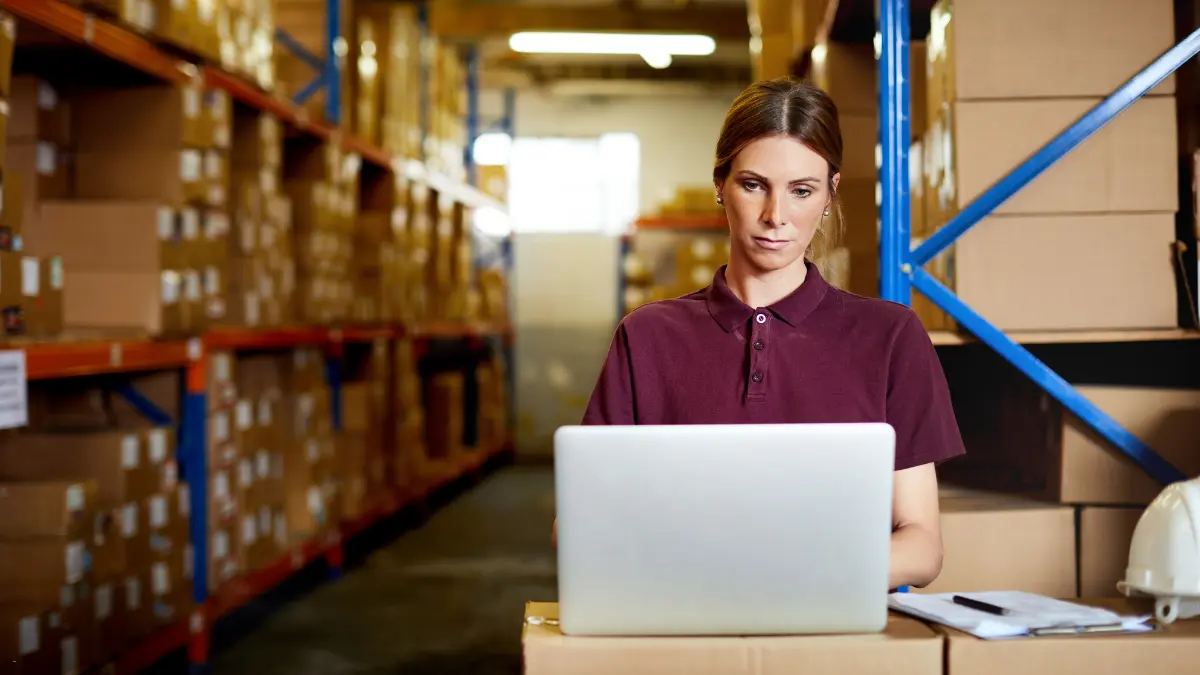 Supplier compliance solutions being utilized by a warehouse manager working on a laptop surrounded by boxes