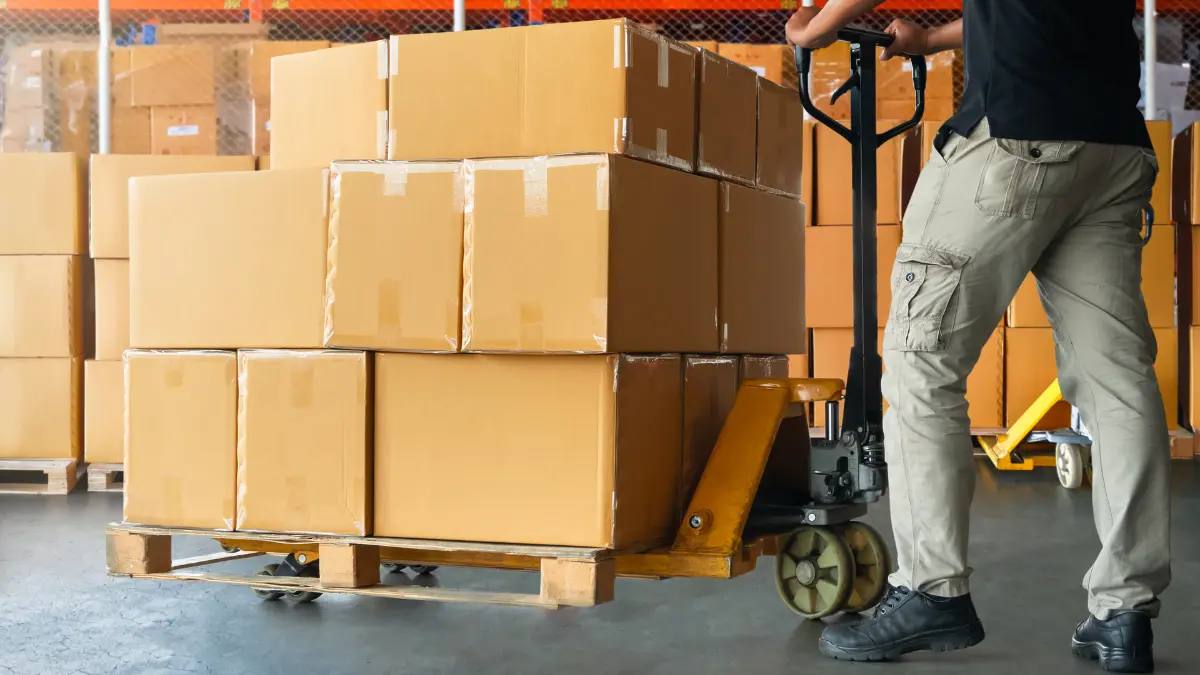 Worker transporting stacked cardboard boxes on a pallet jack, representing supplier risk assessment in logistics.