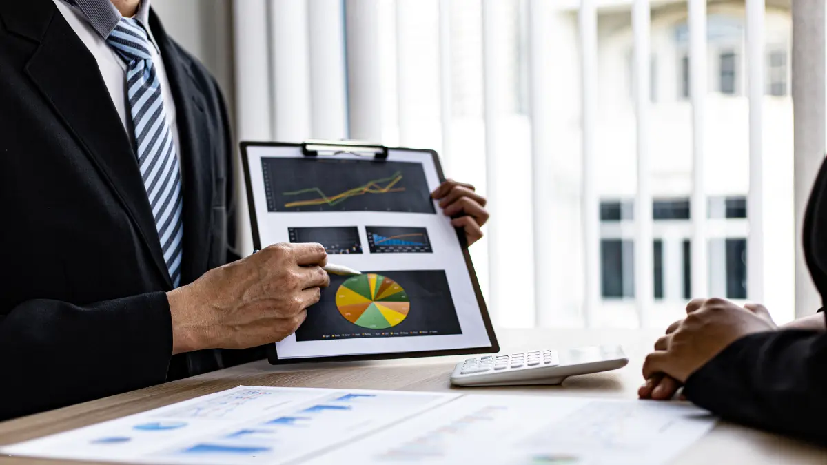 Third-party risk management regulations explained using charts and graphs on a clipboard during a business meeting.