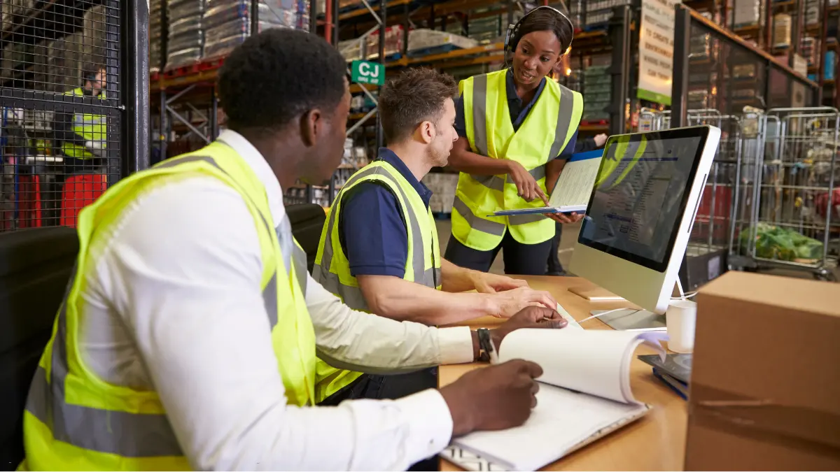 Vendor risk management team reviewing logistics data on a computer in a warehouse setting.
