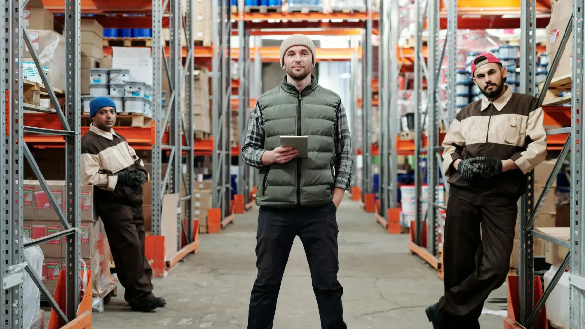 Vendor risk management strategies coordinated by warehouse staff using digital devices among packed shelves.