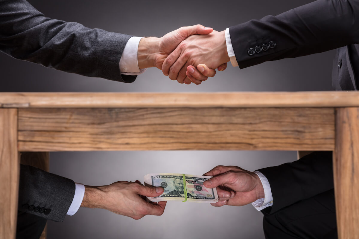 Entrepreneurs shaking hands while taking bills under a table