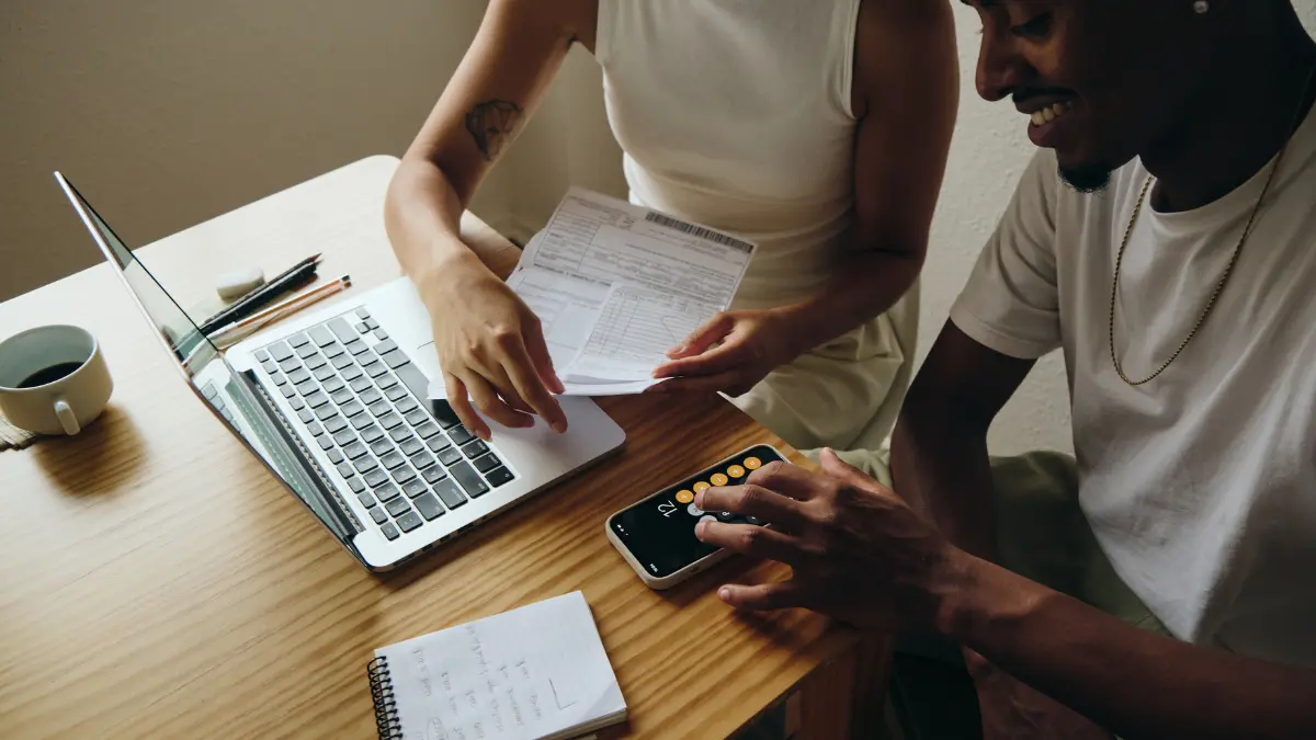 hird-party audit automation discussion over invoices and calculations with a laptop and smartphone on a wooden desk.