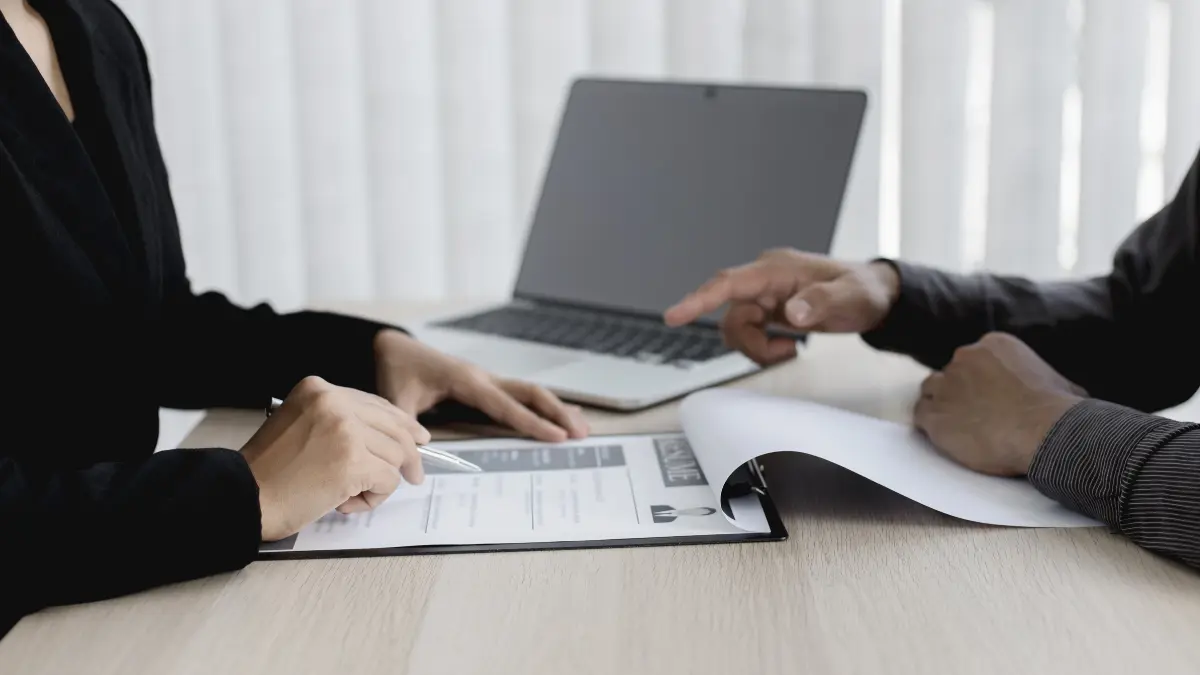 Risk and compliance framework discussion between two professionals reviewing documents beside a laptop.