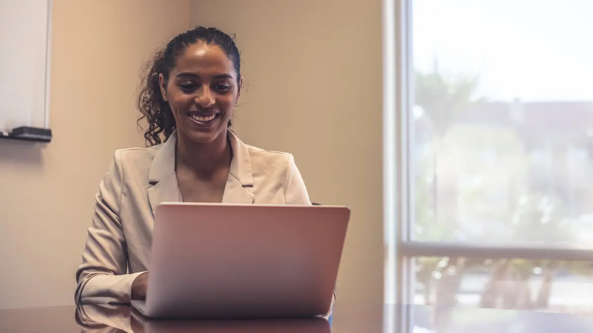 Third-party risk management services specialist smiling while using a laptop in a bright meeting room