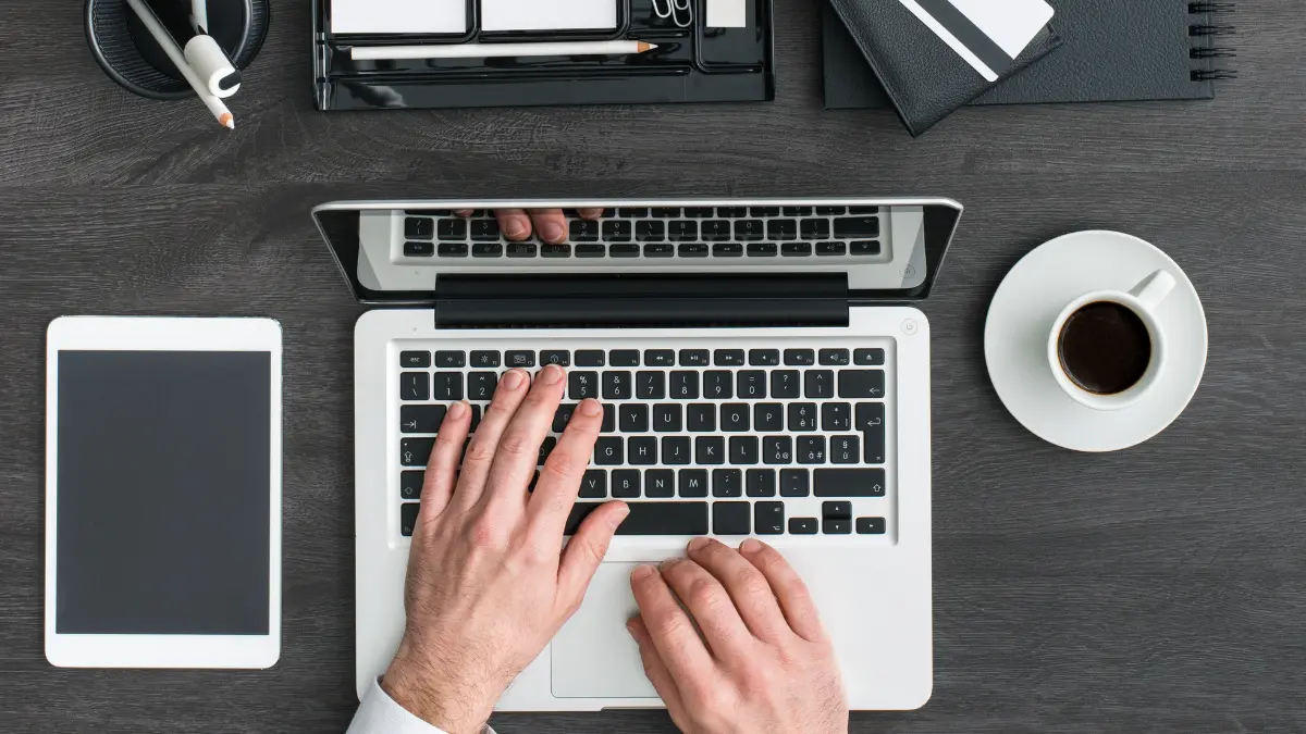 Net zero strategies analyzed by a person working on a laptop with a tablet, coffee, and organized desk items.