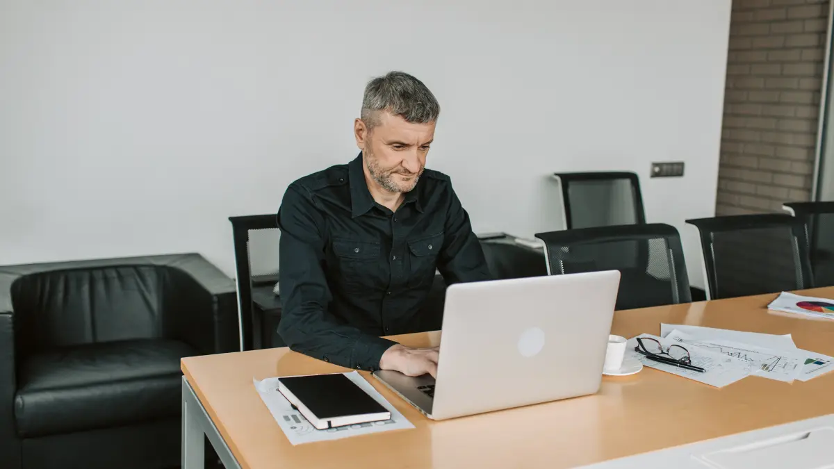 Scope 4 reporting reviewed by a man using a laptop in a modern office with documents and charts on the table.