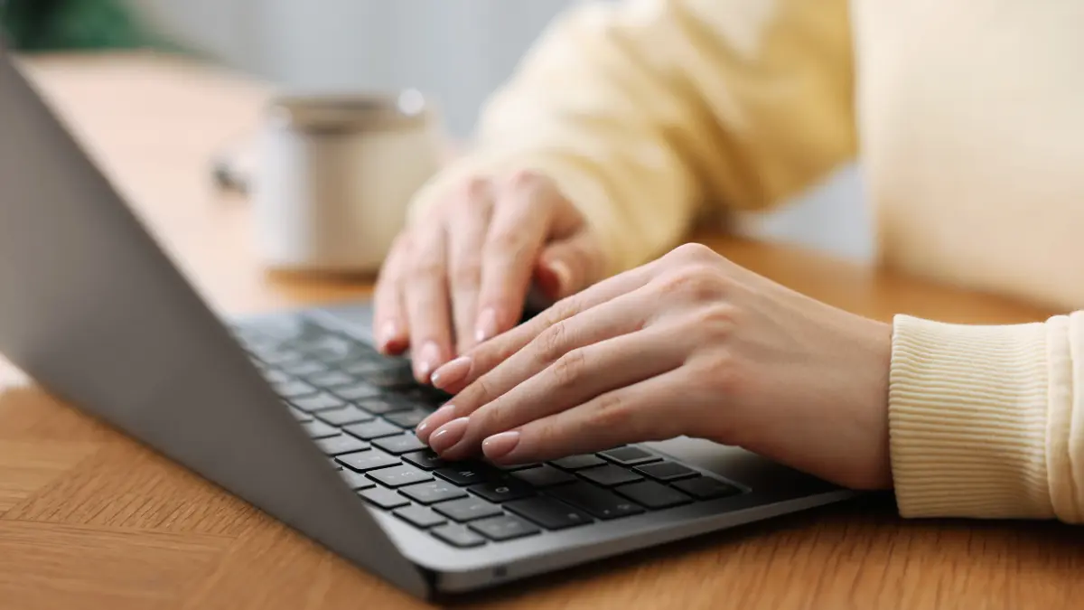 Climate action plans typed on a laptop by a person in a yellow sweater at a wooden desk with a coffee mug.