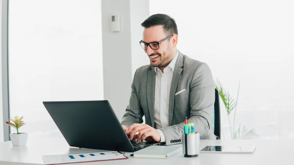 ESG risk management work conducted by a smiling businessman in a gray suit at a bright office desk.