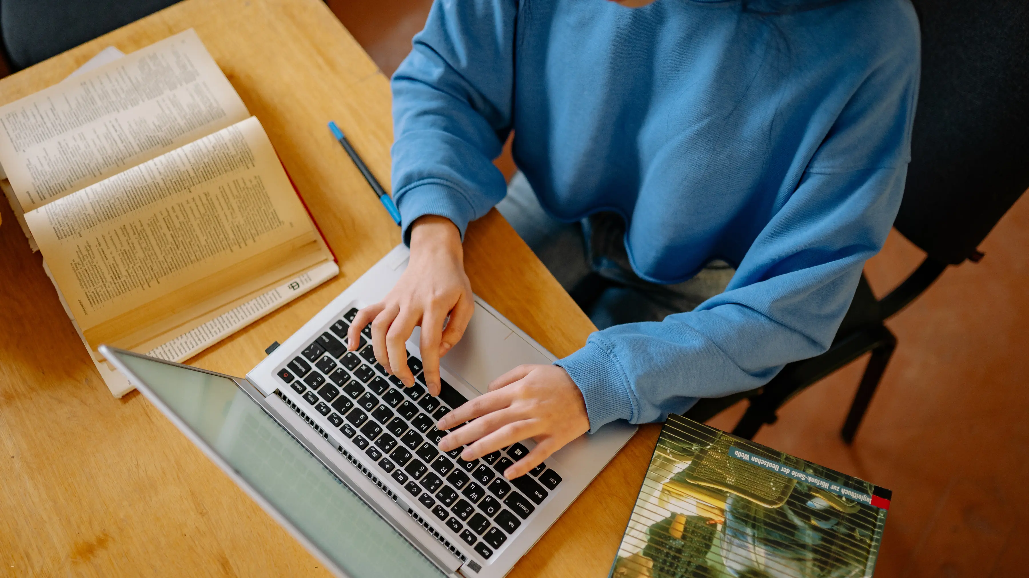third party risk management software: Third party risk management software shown with a person working on a laptop beside open books at a desk, representing research, compliance, and digital risk assessment.