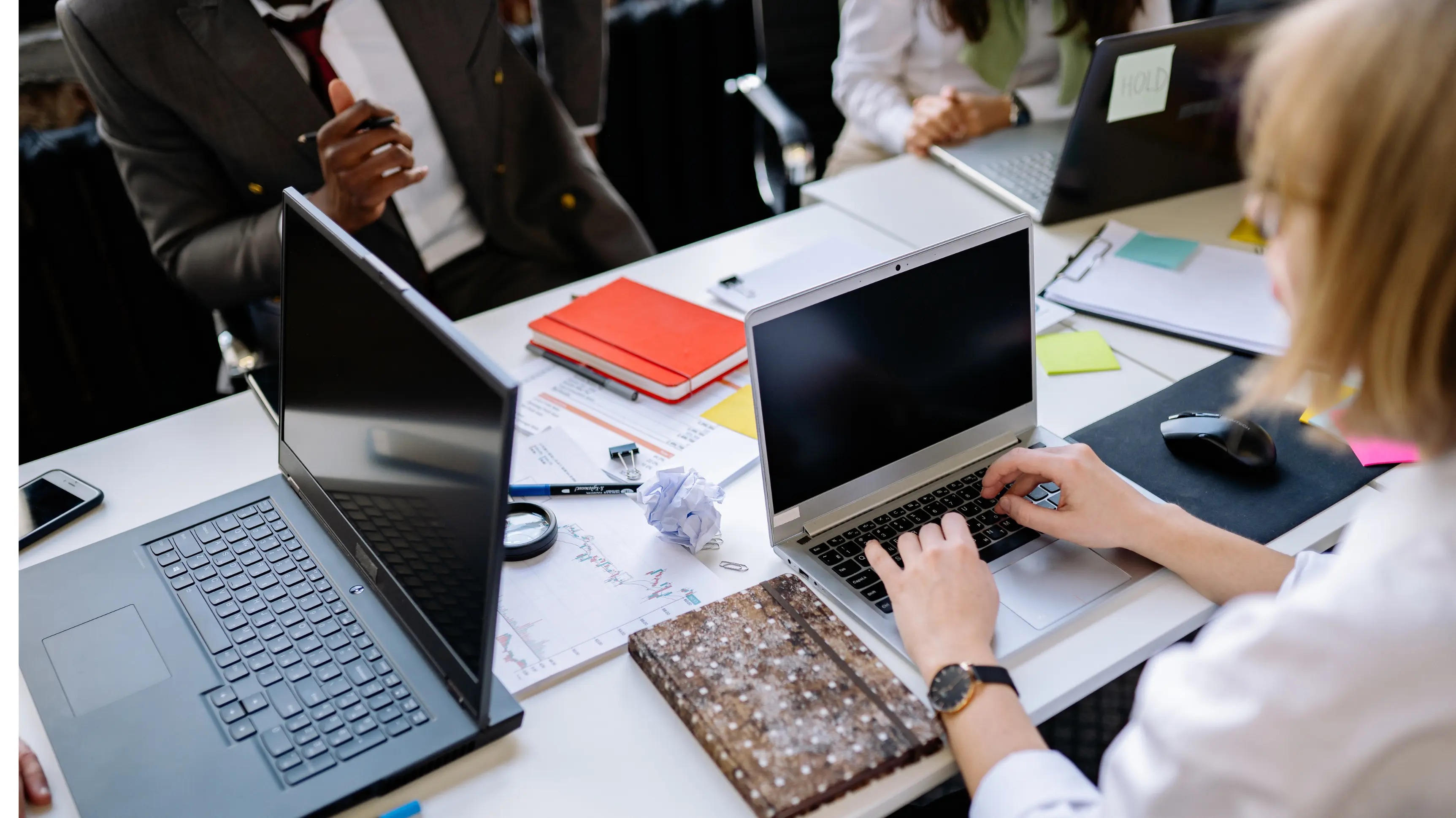 AI risk assessment tools being used by a diverse team of professionals working on multiple laptops surrounded by reports and documents at a shared office desk