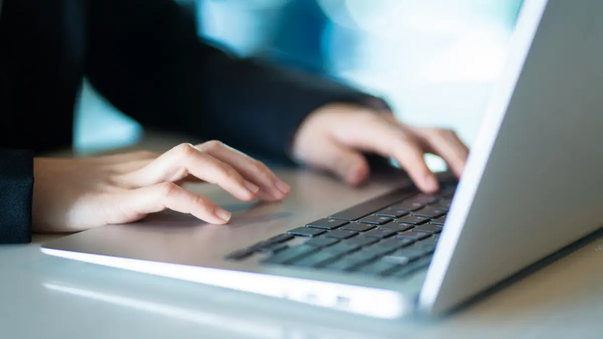 Enterprise risk management professional typing on a laptop in a darkened office setting with blue screen glow.